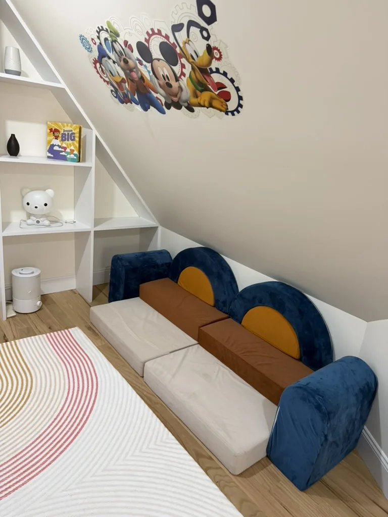 Indoor play den with a soft modular play couch, a mural, and a low bookshelf